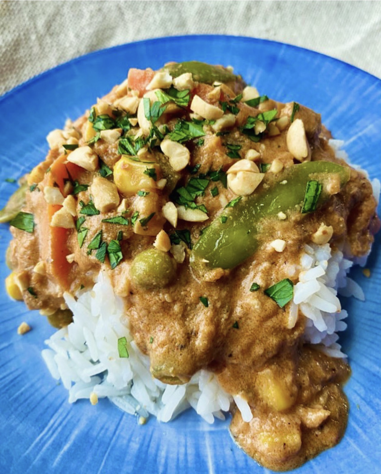Vegan Peanut Butter Stew served over white rice with vegetables and chopped peanuts on a blue plate